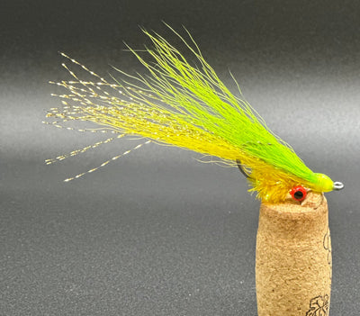 Fishing fly with green body and yellow tail on a cork base against a dark background