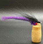 Fishing lure with purple and black fibers on a cork base against a gray background