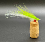 Fishing lure with green and white fibers on a cork base against a dark background