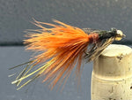 Fishing fly with orange and black feathers on a cork stopper against a gray background