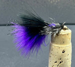 Fishing fly with purple and black feathers on a cork stopper against a gray background