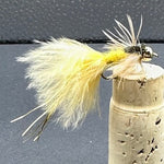 Fishing fly with yellow body and white feathers on a cork block against a dark background