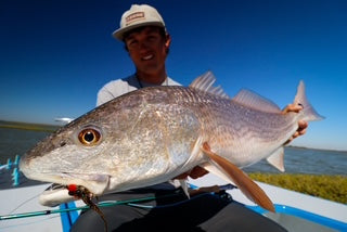 Person holding a large fish on a boat with a clear blue sky and water in the background