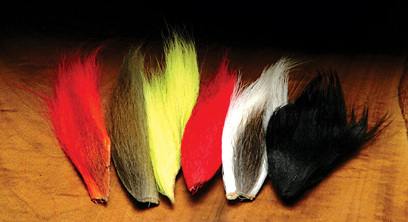 Five bundles of hair in red, yellow, red, white, and black on a wooden surface.